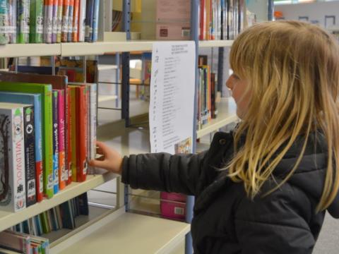 bambina che sceglie un libro in biblioteca